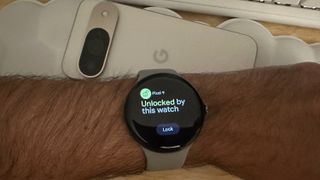 The Pixel Watch 3 with the screen "Pixel 9 Unlocked by this watch" and a "Lock" option, worn on a wrist hovering above the Pixel 9